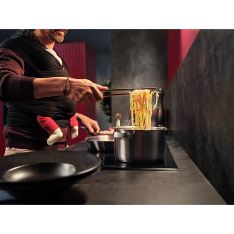 Homme cuisinant des pâtes avec bébé en porte-bébé